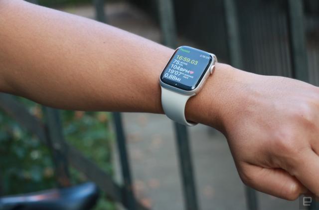 The Apple Watch Series 8 on the wrist of an arm held up in mid-air with a bike seat in the background.