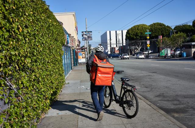 San Francisco, CA, USA - Feb 8, 2020: A DoorDash delivery worker walks his bike along the road in the Mission neighborhood of San Francisco, California.