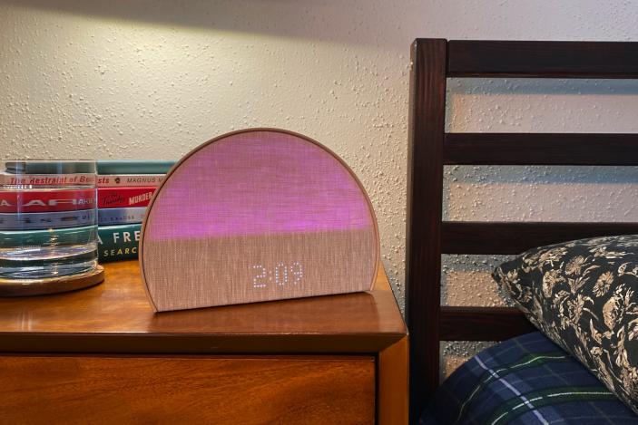 The Hatch Restore 2 sleep machine sits on my bedside table. There's a glass of water and a stack of books in the background. The bed's headboard and pillow are to the right of the image. 