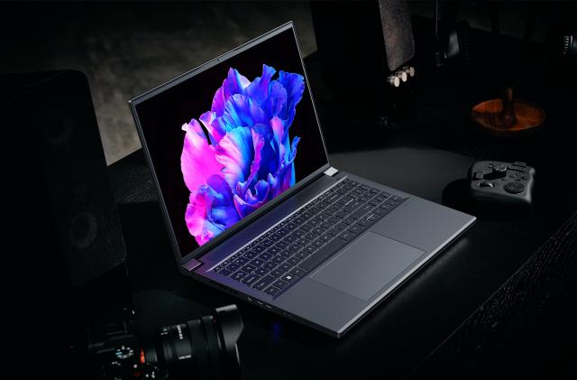 Acer Swift X 16 Promotional Image, with the Swift X sat on a dark table shrouded in darkness, the hint of a drone controller and a DSLR lurking in the gloom.