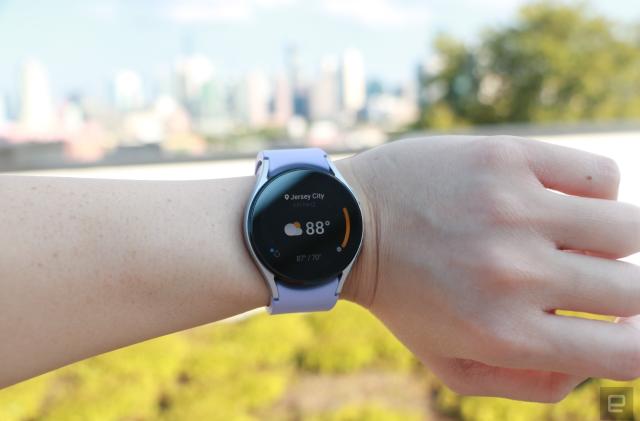 The Samsung Galaxy Watch 5 on a wrist, showing the weather app. It says Jersey City at the top, followed by 88 degrees in bigger font taking up the majority of the page, and a cloud with sun icon on its left.