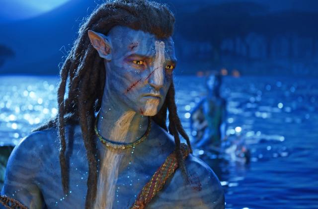 A closeup of Jake Sully in 20th Century Studios' AVATAR: THE WAY OF WATER with a large lake in the background.