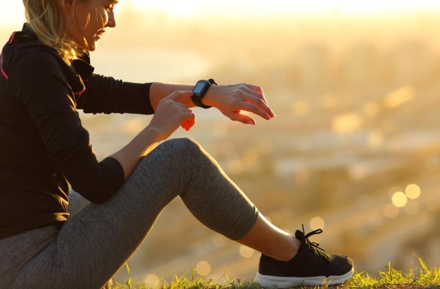 Runner sitting on the ground checking smartwatch after running at sunset