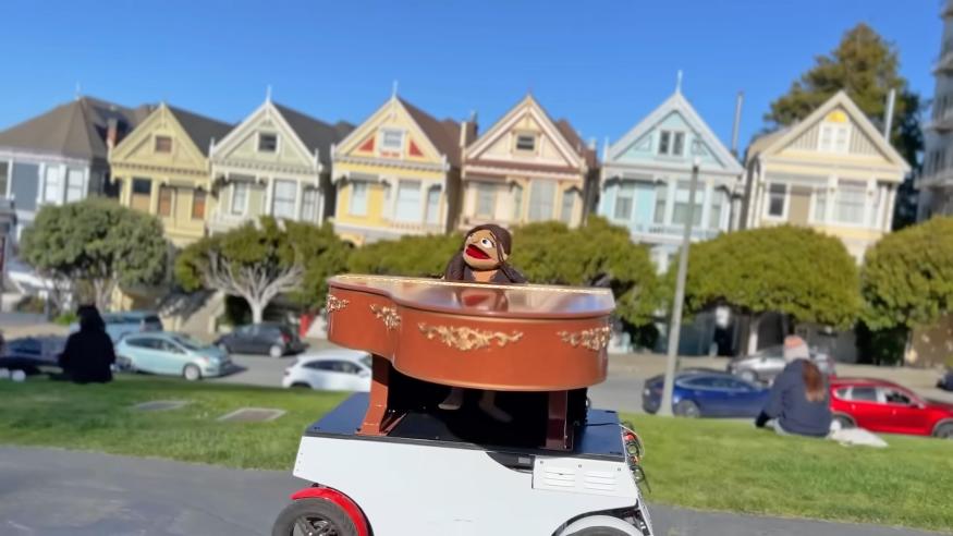 The muppetized Vanessa Carlton robot in a small wheeled vehicle with a piano on Steiner St in San Francisco.