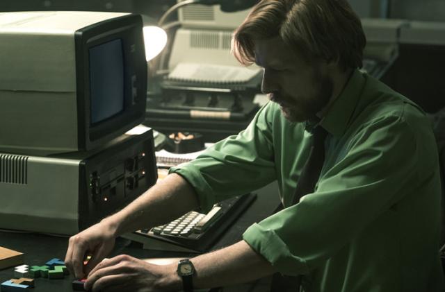 Alexey Pajitnov (Nikita Efremov) moves some Tetris-style blocks around in a desk next to an old computer in the movie 'Tetris.'