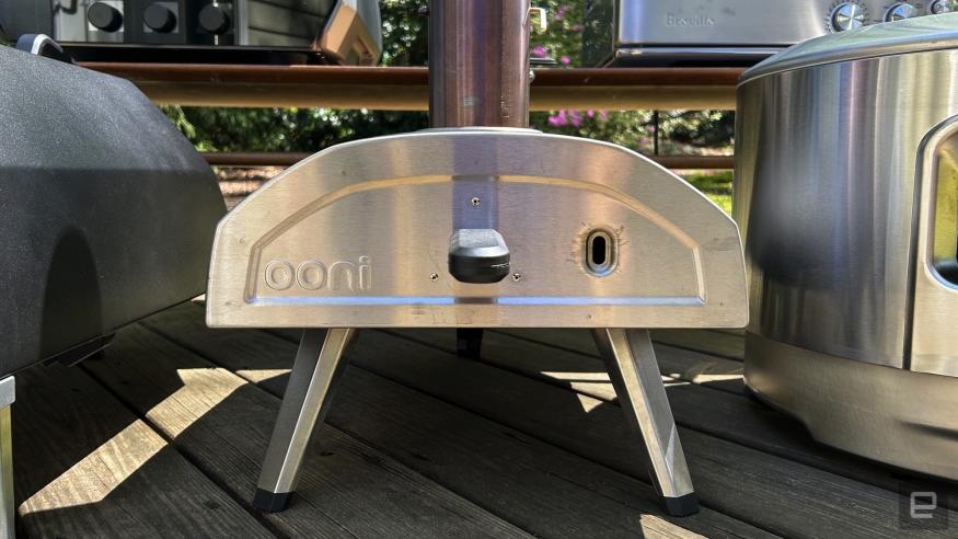 An Ooni Fyra 12 pizza oven in silver sitting on a wood porch. 