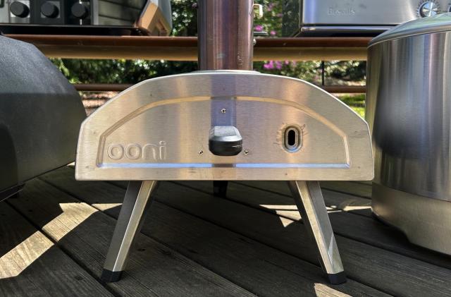 An Ooni Fyra 12 pizza oven in silver sitting on a wood porch. 