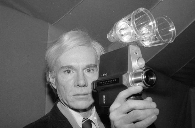 Artist and underground filmmaker Andy Warhol poses with one of Polaroid's new film cameras, the Polavision camera, which features instant replay on television screens, Feb. 1, 1978. (AP Photo/Dave Pickoff)