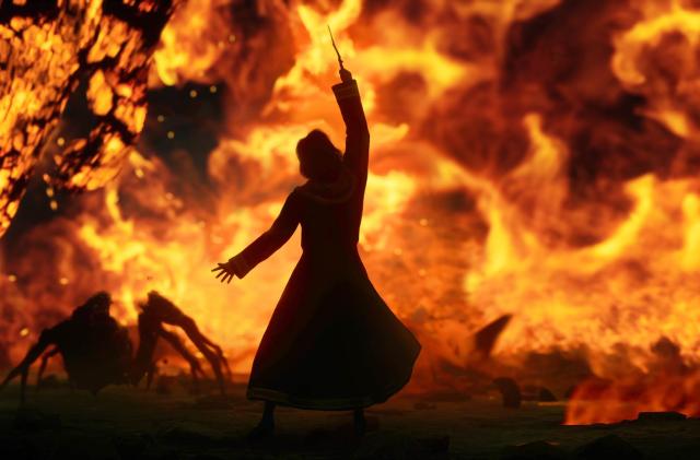 In this screenshot from the video game Hogwarts Legacy, a wizard or witch stands in front of a wall of fire and lifts their wand to the sky, while an acromantula scurries in the midground.